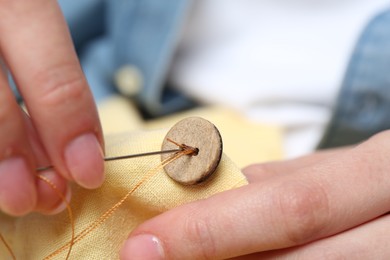 Photo of Woman sewing button with needle and thread onto shirt, closeup