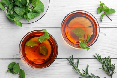 Photo of Cups of aromatic herbal tea with mint and rosemary on white wooden table, flat lay