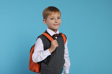 Happy schoolboy with backpack on light blue background