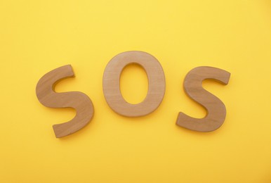 Photo of Abbreviation SOS made of wooden letters on yellow background, top view