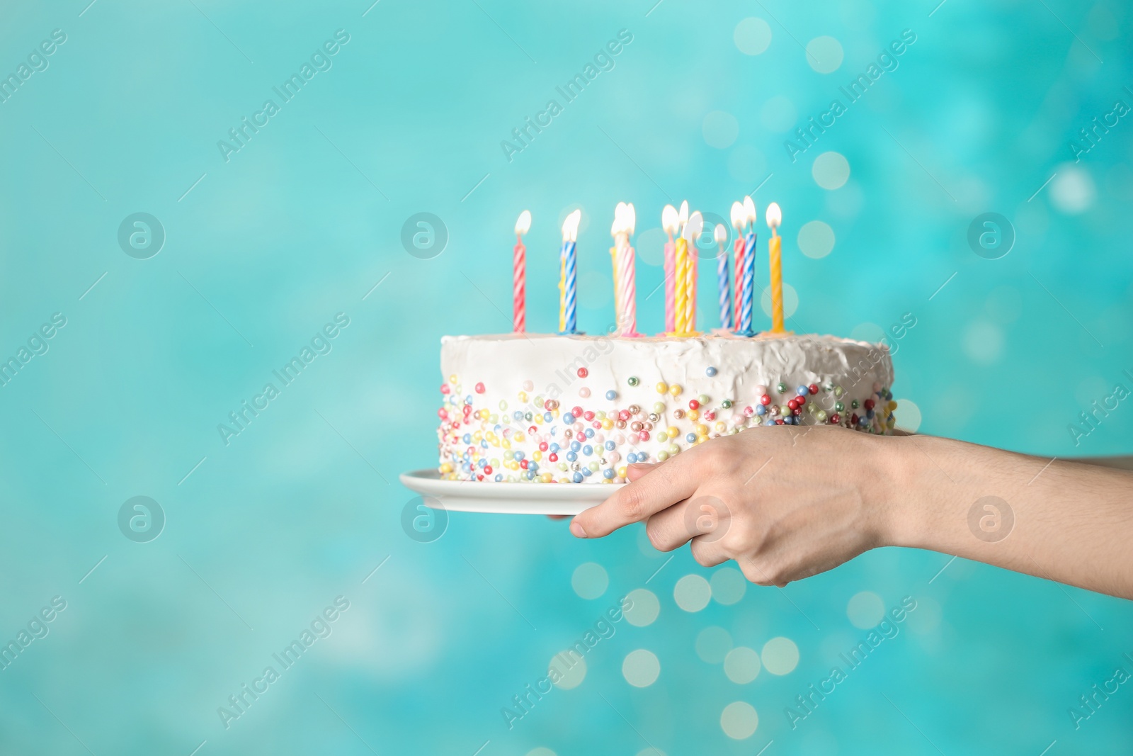 Photo of Woman holding birthday cake with burning candles on light blue background, closeup