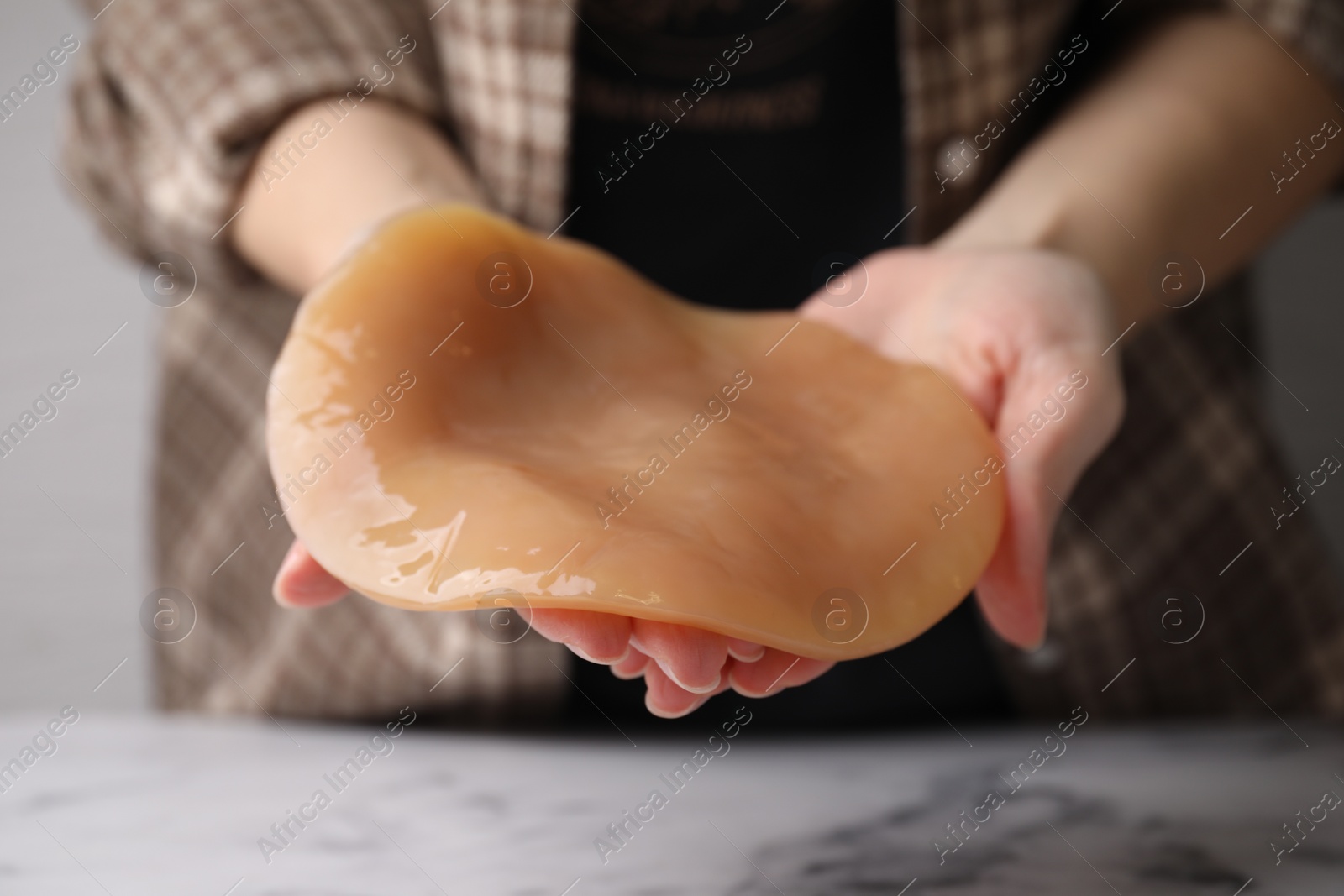 Photo of Making kombucha. Woman holding Scoby fungus at table, closeup