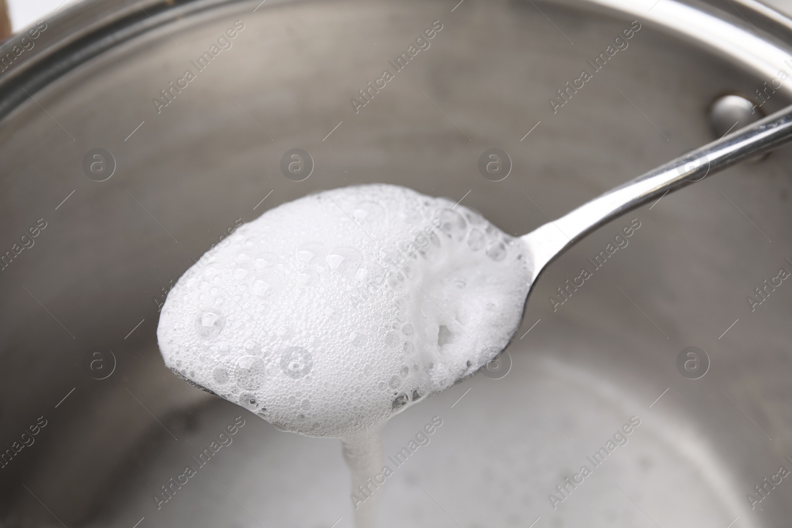 Photo of Chemical reaction of vinegar and baking soda in spoon over saucepan, closeup