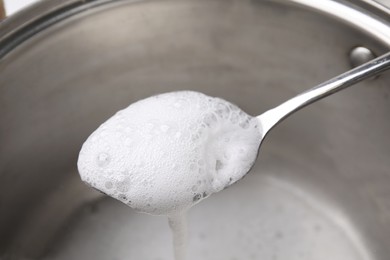 Chemical reaction of vinegar and baking soda in spoon over saucepan, closeup