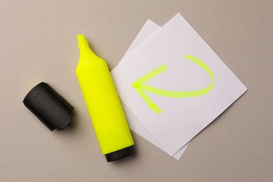 Photo of Bright yellow marker and sticky note with drawn arrow on light grey background, flat lay