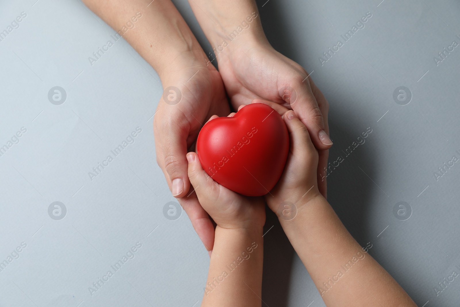 Photo of Mother and her child holding red decorative heart on gray background, top view