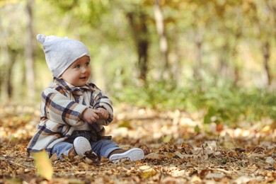 Photo of Cute little child on ground with dry leaves in autumn park, space for text