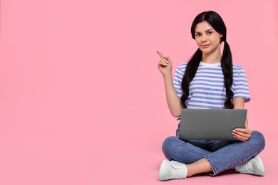 Photo of Student with laptop pointing at something on pink background. Space for text