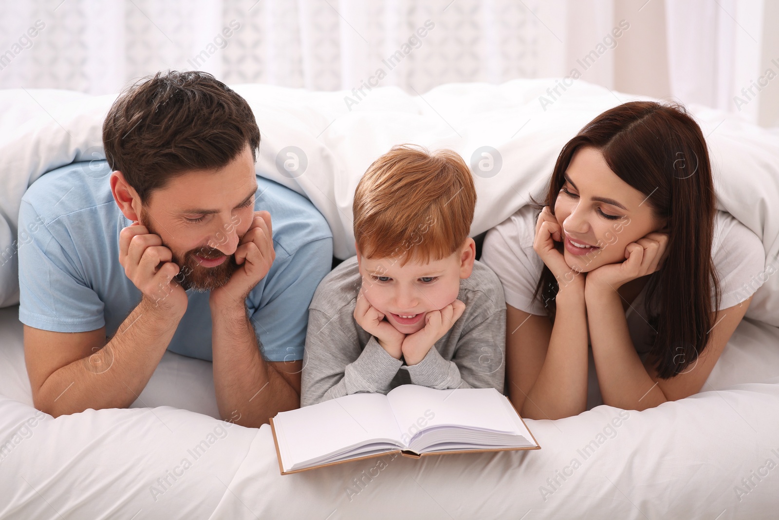 Photo of Happy parents with their child reading book on bed at home