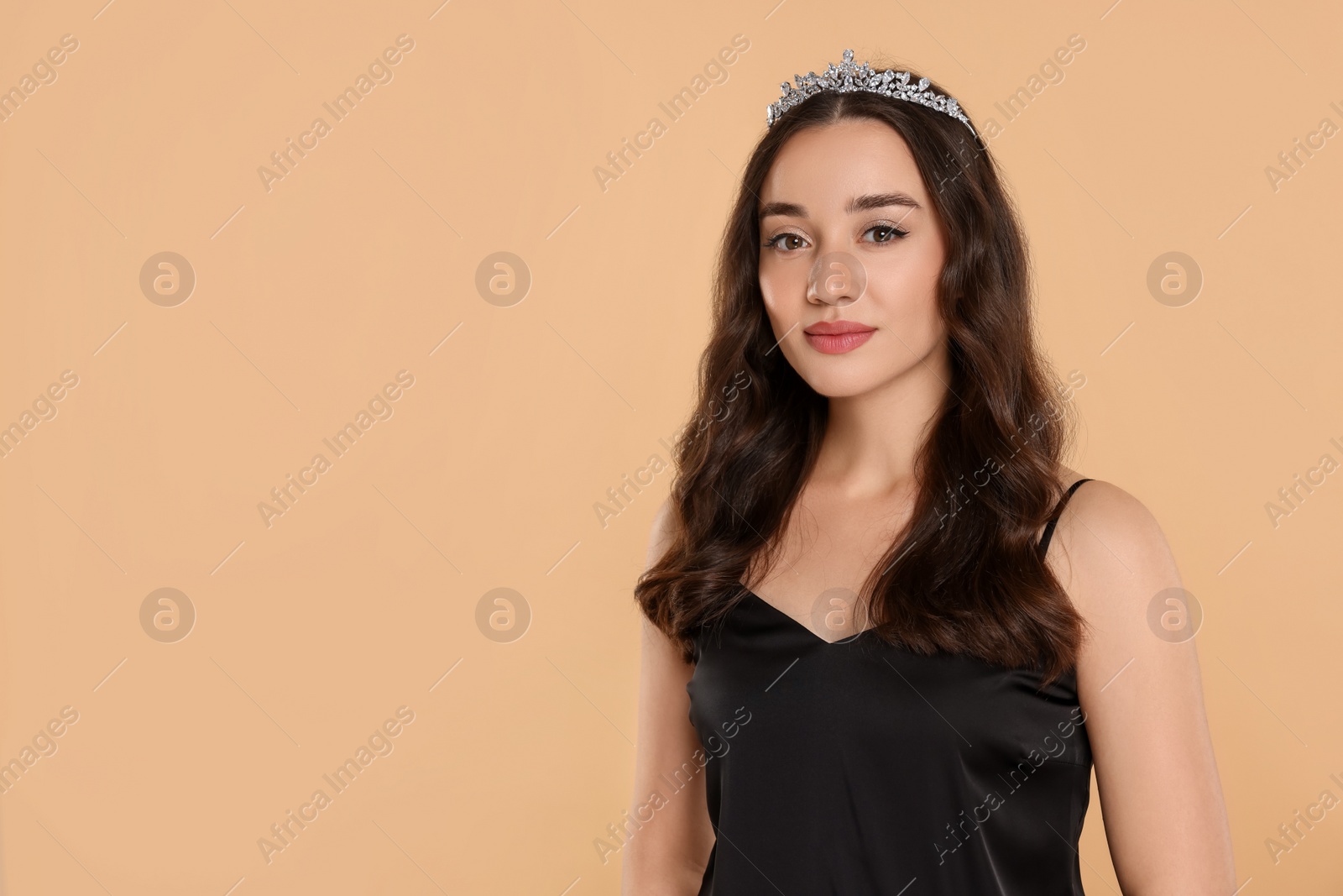 Photo of Beautiful young woman with tiara in stylish dress on beige background, space for text