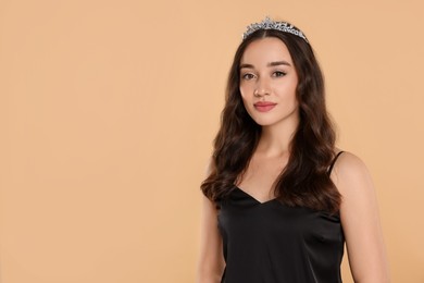 Photo of Beautiful young woman with tiara in stylish dress on beige background, space for text