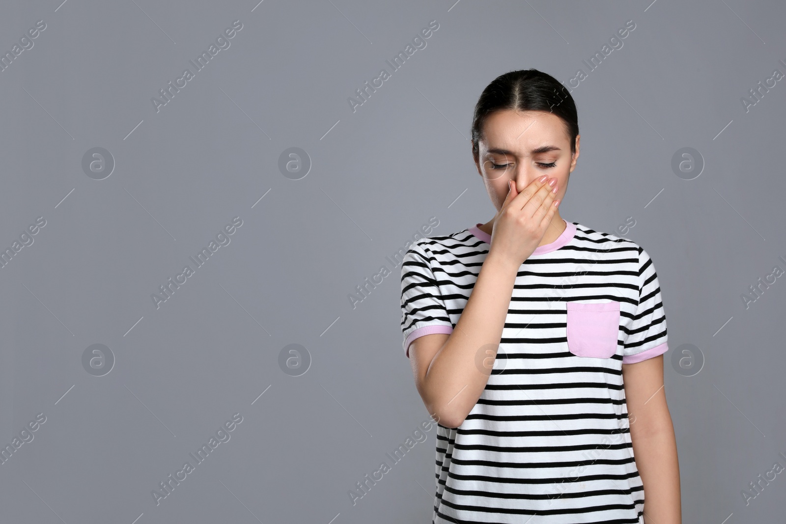 Photo of Young woman suffering from cold on grey background, space for text