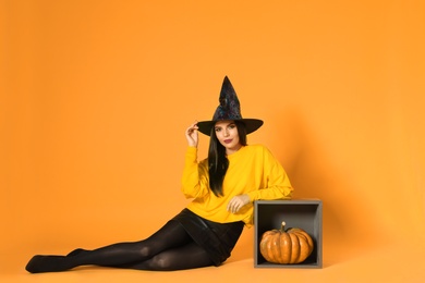 Beautiful woman wearing witch costume for Halloween party on yellow background