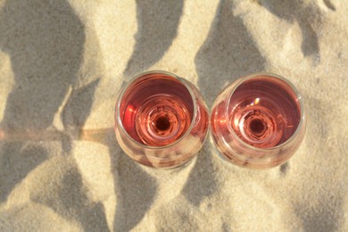 Photo of Glassestasty rose wine on sand, top view