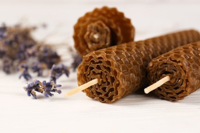 Stylish elegant beeswax candles and lavender on white wooden table, closeup