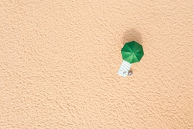 Image of Beach umbrella near towel and other vacationist's stuff on sand, aerial view. Space for text