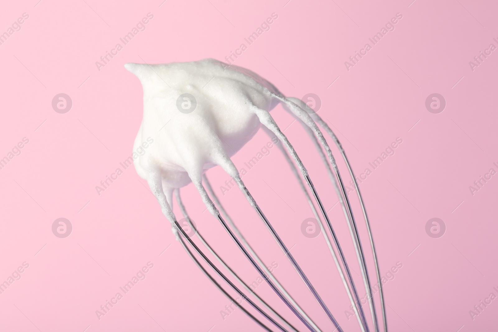 Photo of Whisk with whipped egg whites on pink background, closeup