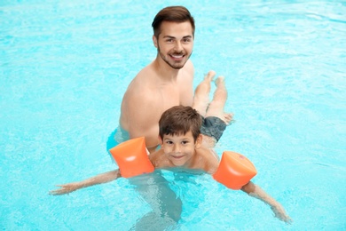Photo of Father teaching son to swim with inflatable sleeves in pool