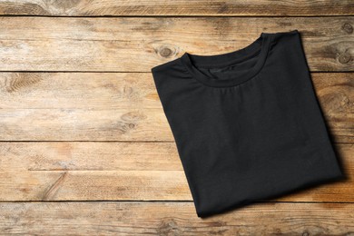 Photo of Stylish black T-shirt on wooden table, top view. Space for text