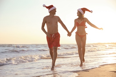 Photo of Happy couple with Santa hats together on beach. Christmas vacation