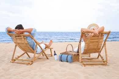 Happy young couple sitting on deck chairs at sea beach