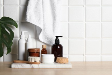 Different bath accessories and personal care products on wooden table near white tiled wall, space for text