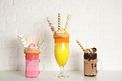 Photo of Tasty milk shakes with sweets in glassware on table near brick wall