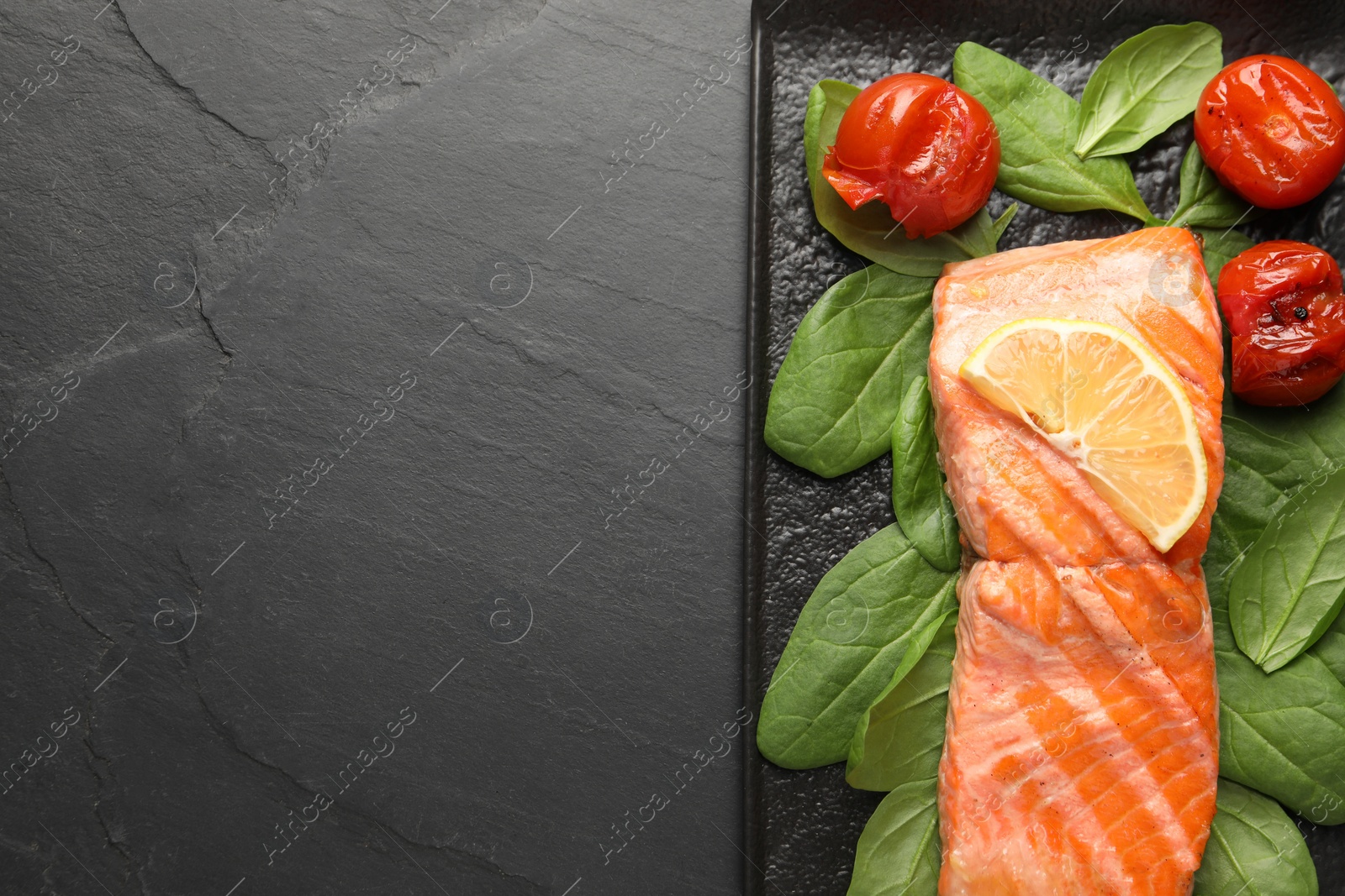 Photo of Tasty grilled salmon with tomatoes, spinach and lemon on black table, top view. Space for text