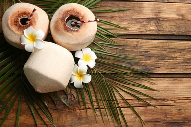 Photo of Fresh coconuts with drinking straws and flowers on wooden table, flat lay. Space for text