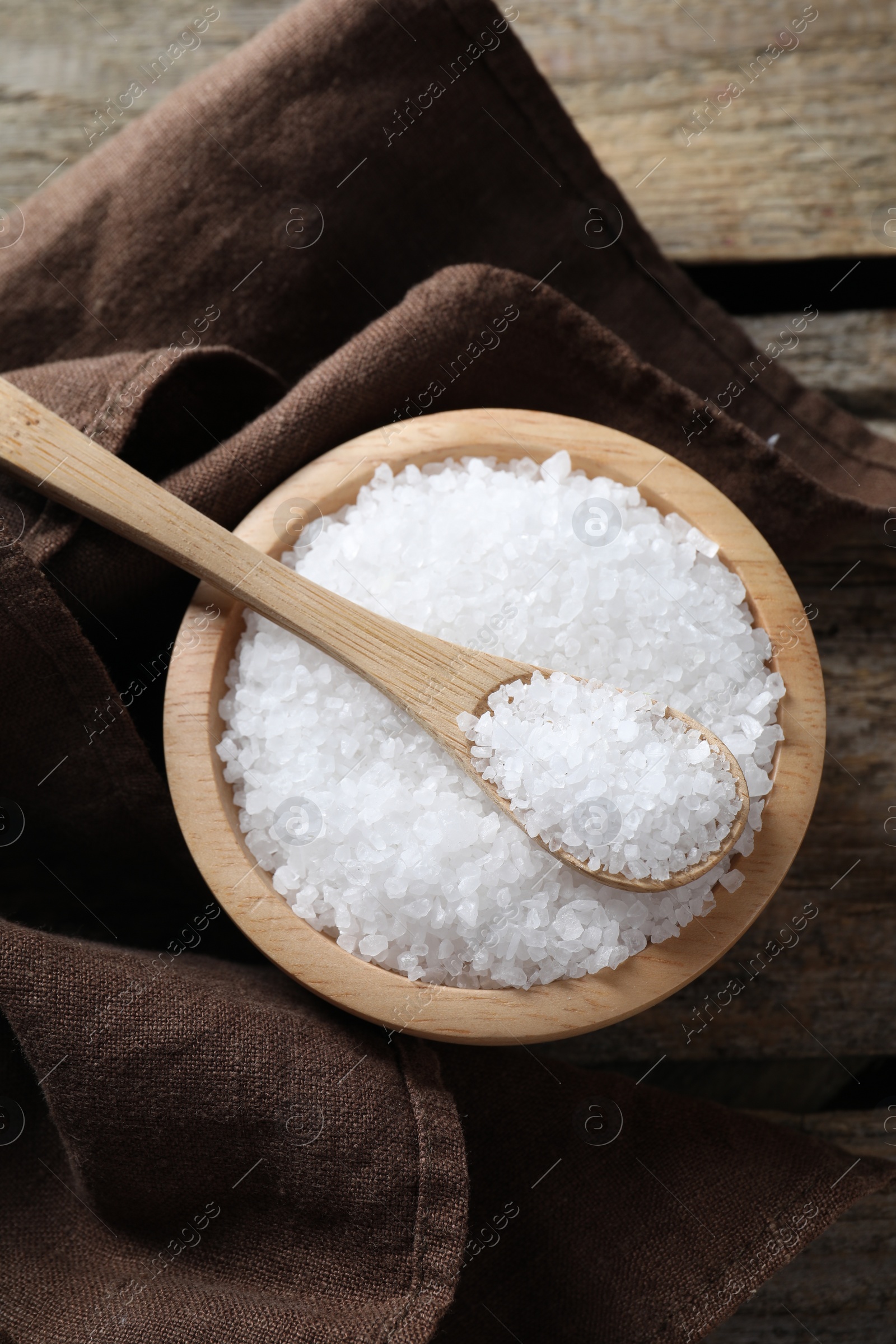 Photo of Organic salt in bowl and spoon on wooden table, top view