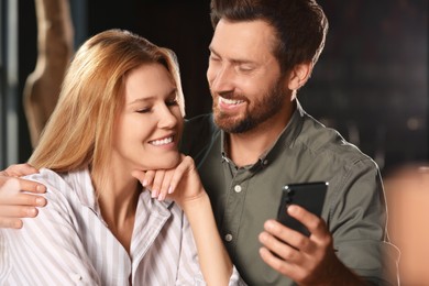 Photo of Romantic date. Happy couple with smartphone spending time together indoors