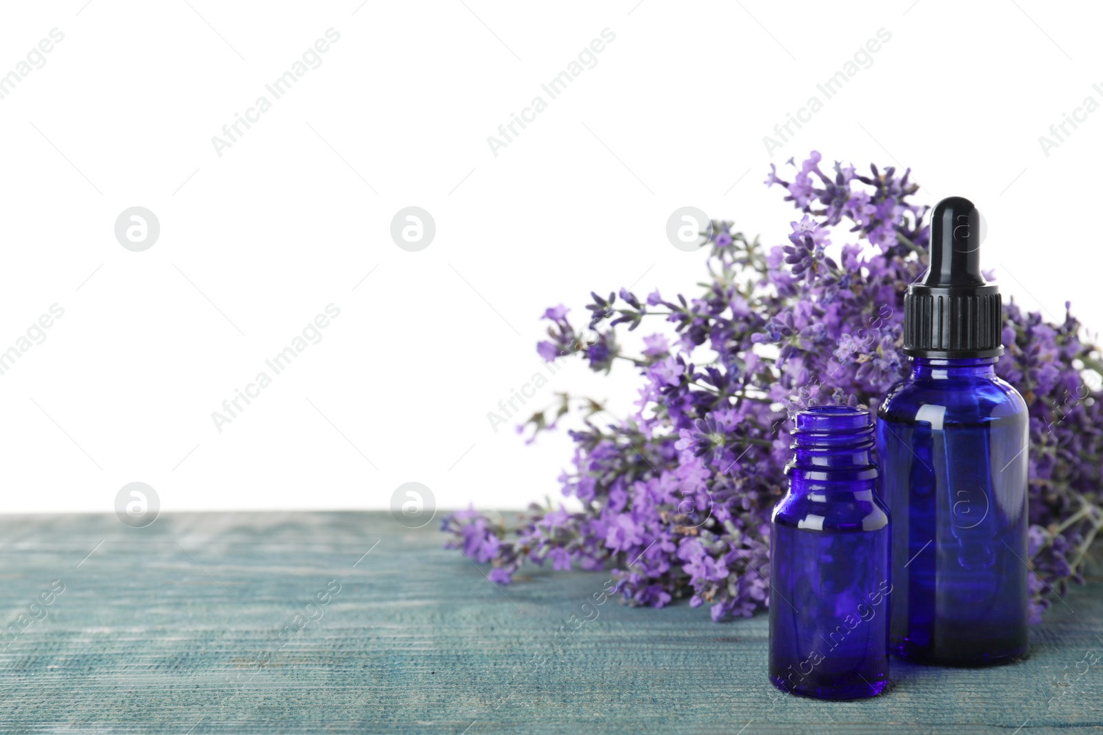 Photo of Bottles of essential oil and lavender flowers on blue wooden table against white background