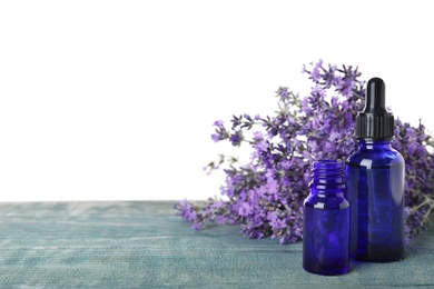 Photo of Bottles of essential oil and lavender flowers on blue wooden table against white background