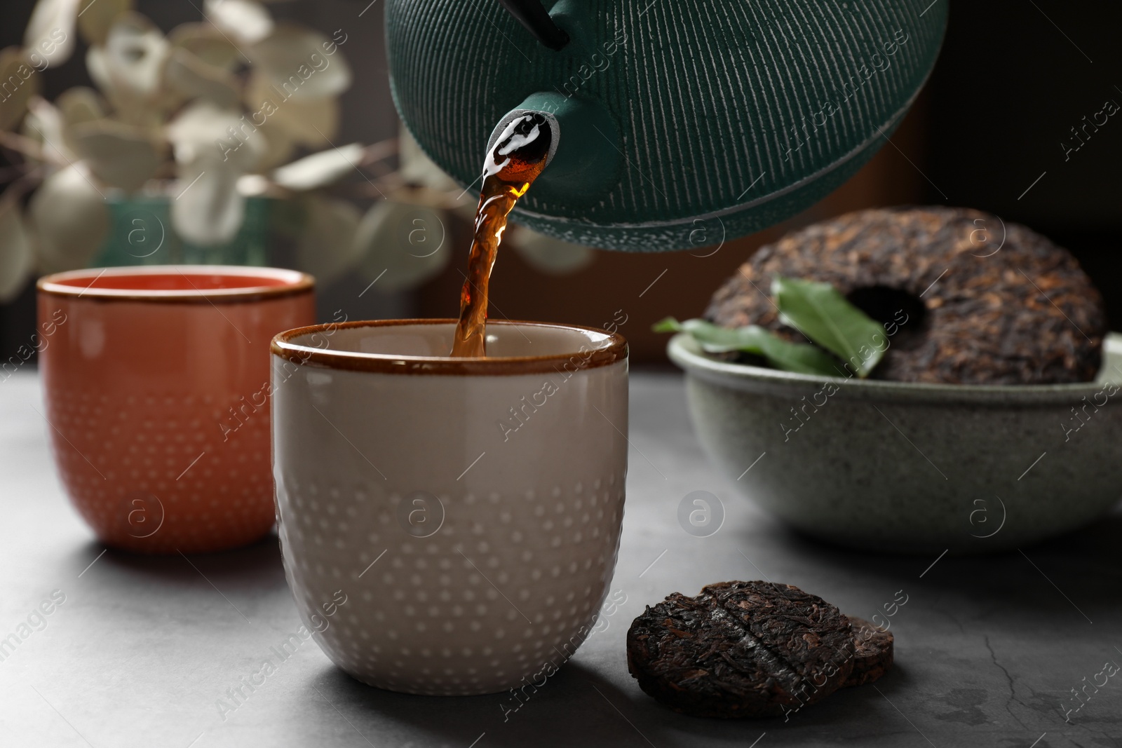 Photo of Pouring freshly brewed pu-erh tea into cup on grey table, closeup