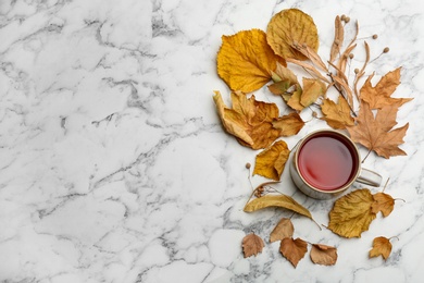 Flat lay composition with cup of hot drink and autumn leaves on white marble background, space for text. Cozy atmosphere