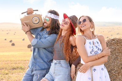 Photo of Happy hippie friends with radio receiver near hay bale in field