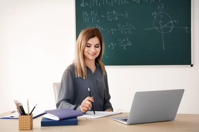 Young female teacher working at table in classroom