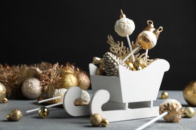 Photo of Delicious Christmas themed cake pops and festive decor on wooden table against black background