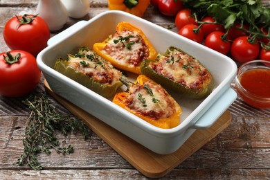 Photo of Tasty stuffed peppers in dish and ingredients on wooden table