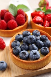 Photo of Tartlets with different fresh berries on board, closeup. Delicious dessert