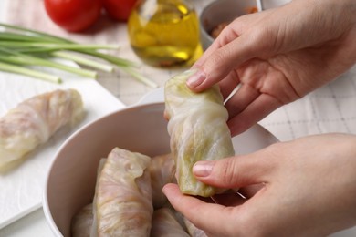Photo of Woman putting uncooked stuffed cabbage roll into ceramic pot at white table, closeup