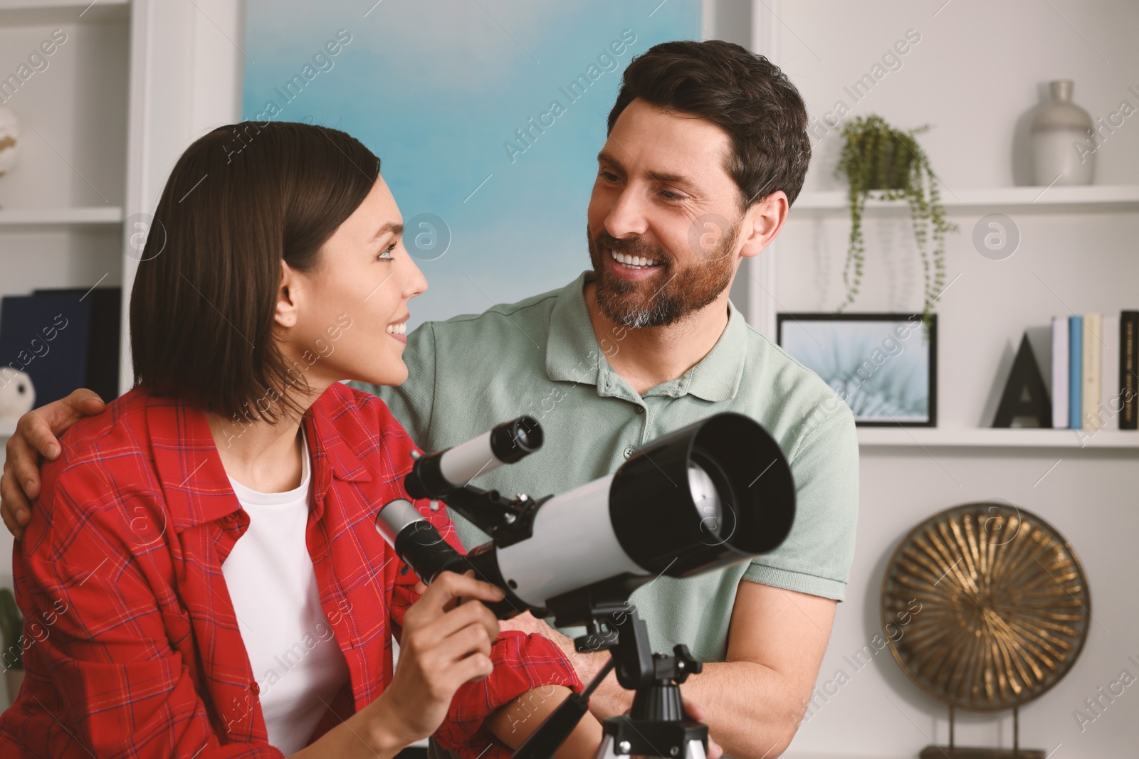 Photo of Happy couple using telescope to look at stars in room