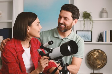 Happy couple using telescope to look at stars in room
