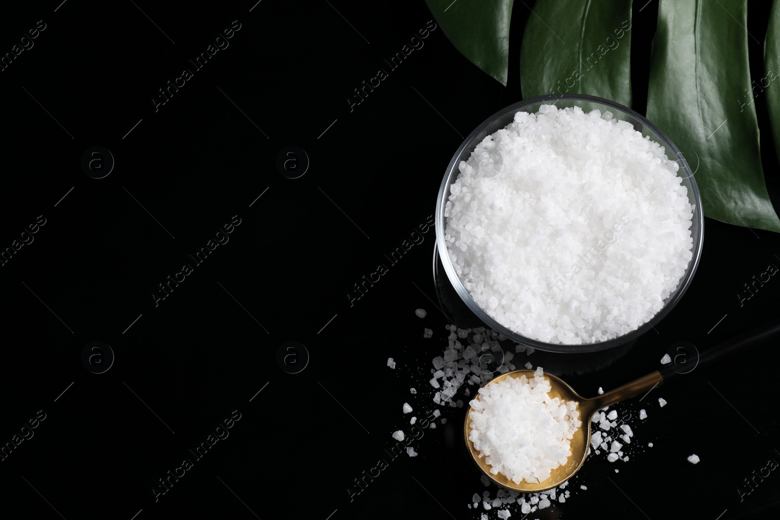 Photo of Bowl and spoon with natural sea salt on mirror table, flat lay. Space for text