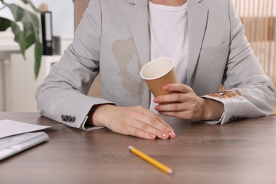 Photo of Woman showing stain from coffee on her jacket at wooden table indoors, closeup