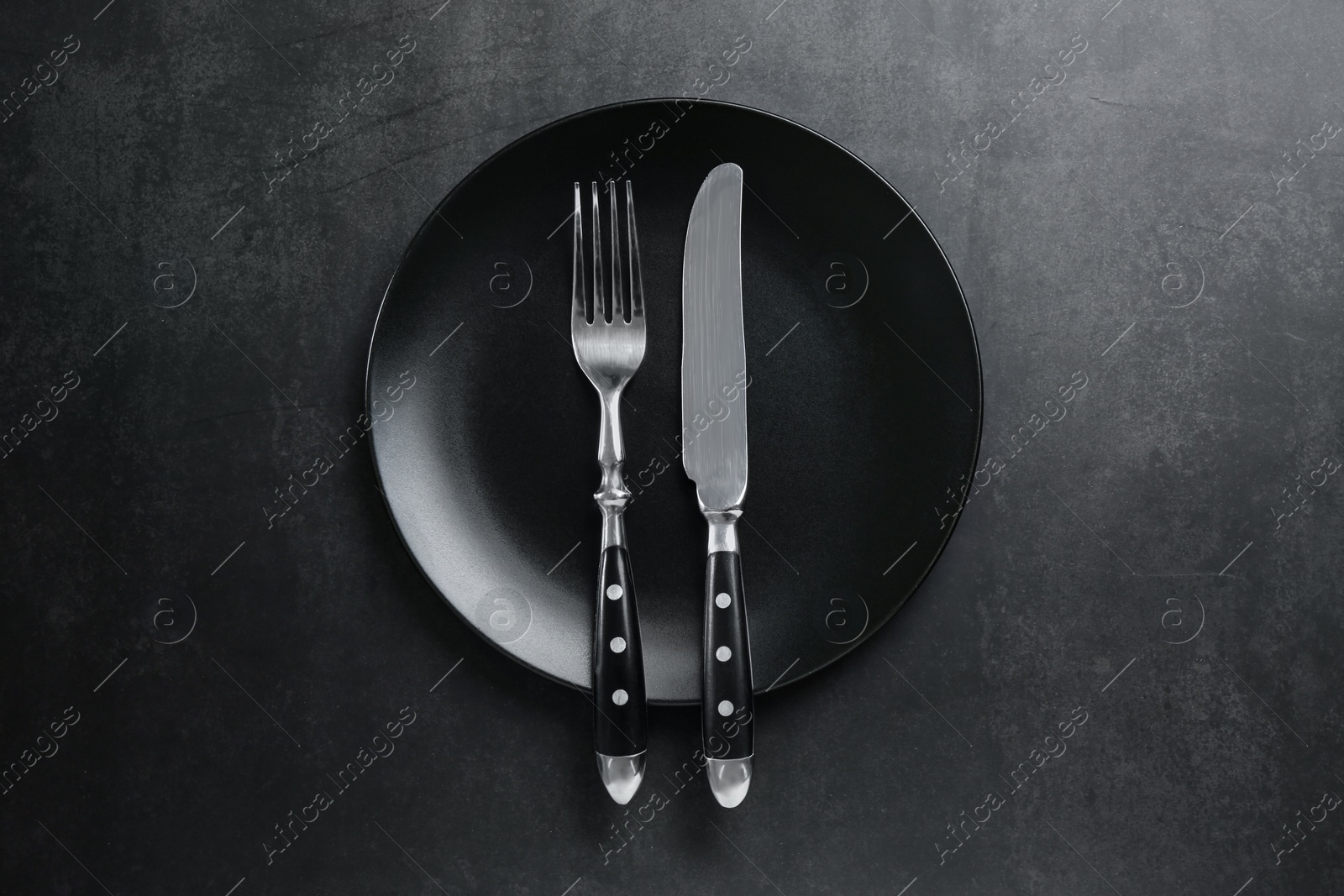 Photo of Ceramic plate, fork and knife on black table, top view