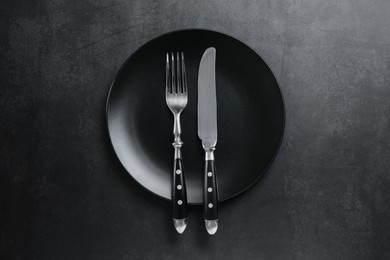 Photo of Ceramic plate, fork and knife on black table, top view