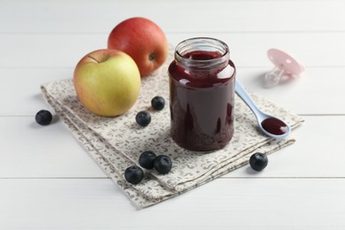 Photo of Tasty baby food in jar, blueberries and apples on white wooden table