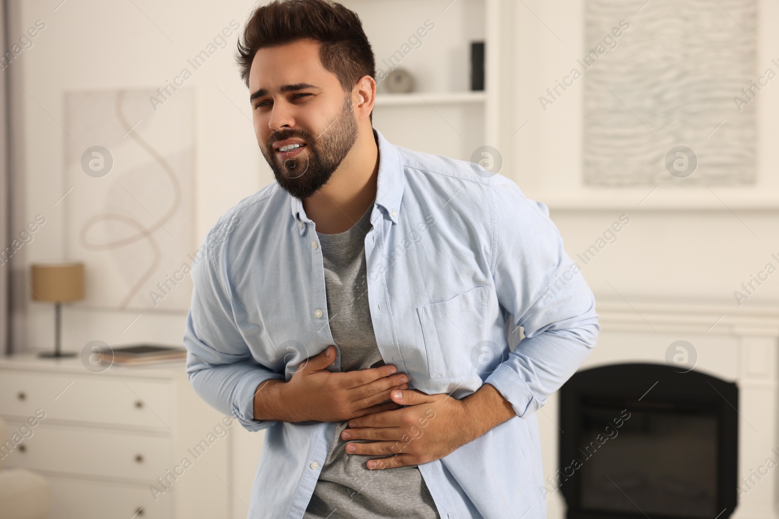 Photo of Young man suffering from stomach pain indoors