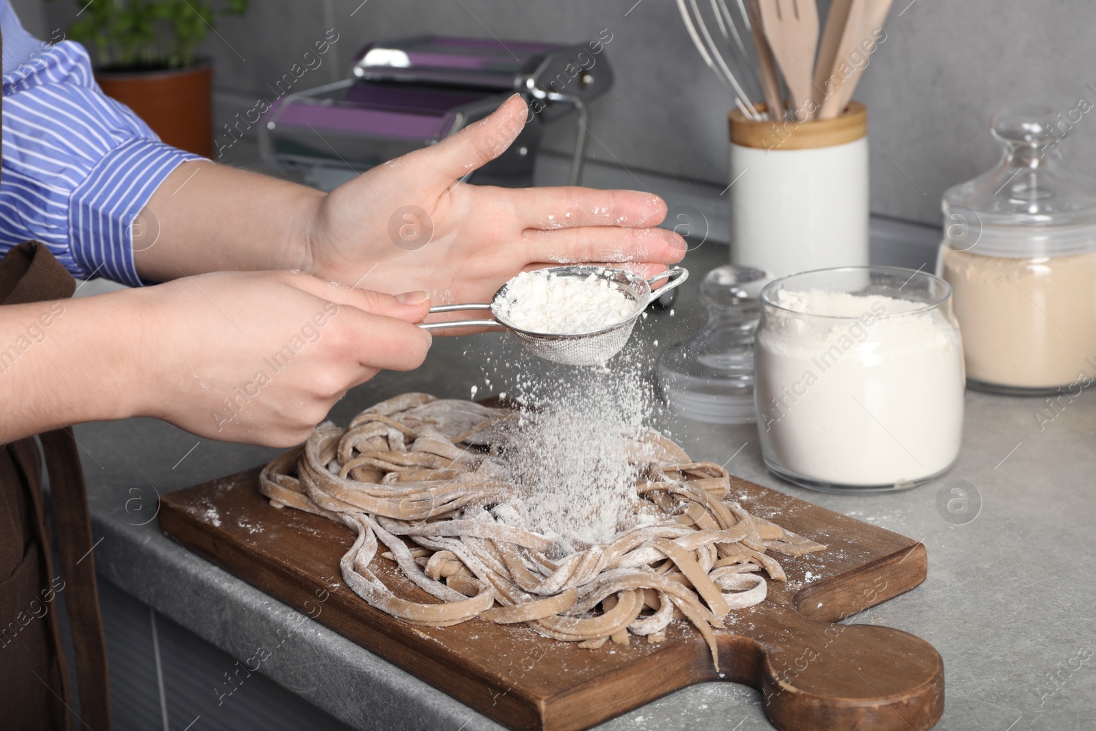 Photo of Woman sprinkling flour over uncooked soba at table in kitchen, closeup